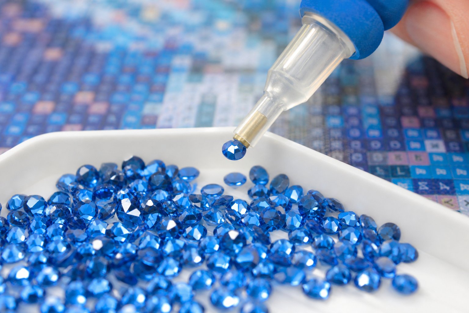 Close-up of a wax-tipped applicator pen lifting a blue resin diamond from a sorting tray during a diamond painting project